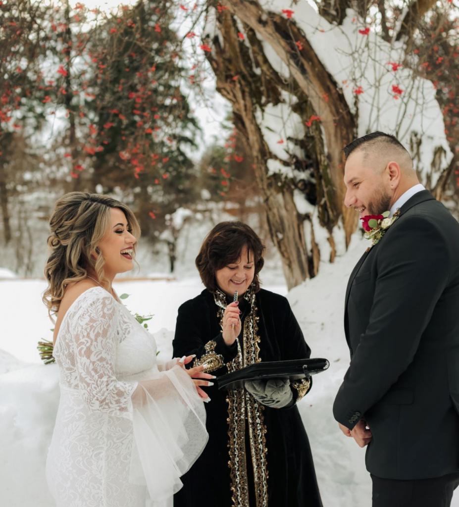 Couple standing smiling in snow with officiant at Christmas elopement while signing the license